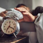 young-man-reaching-for-his-alarm-clock-after-waking-up