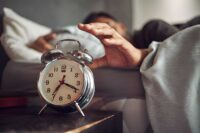 young-man-reaching-for-his-alarm-clock-after-waking-up